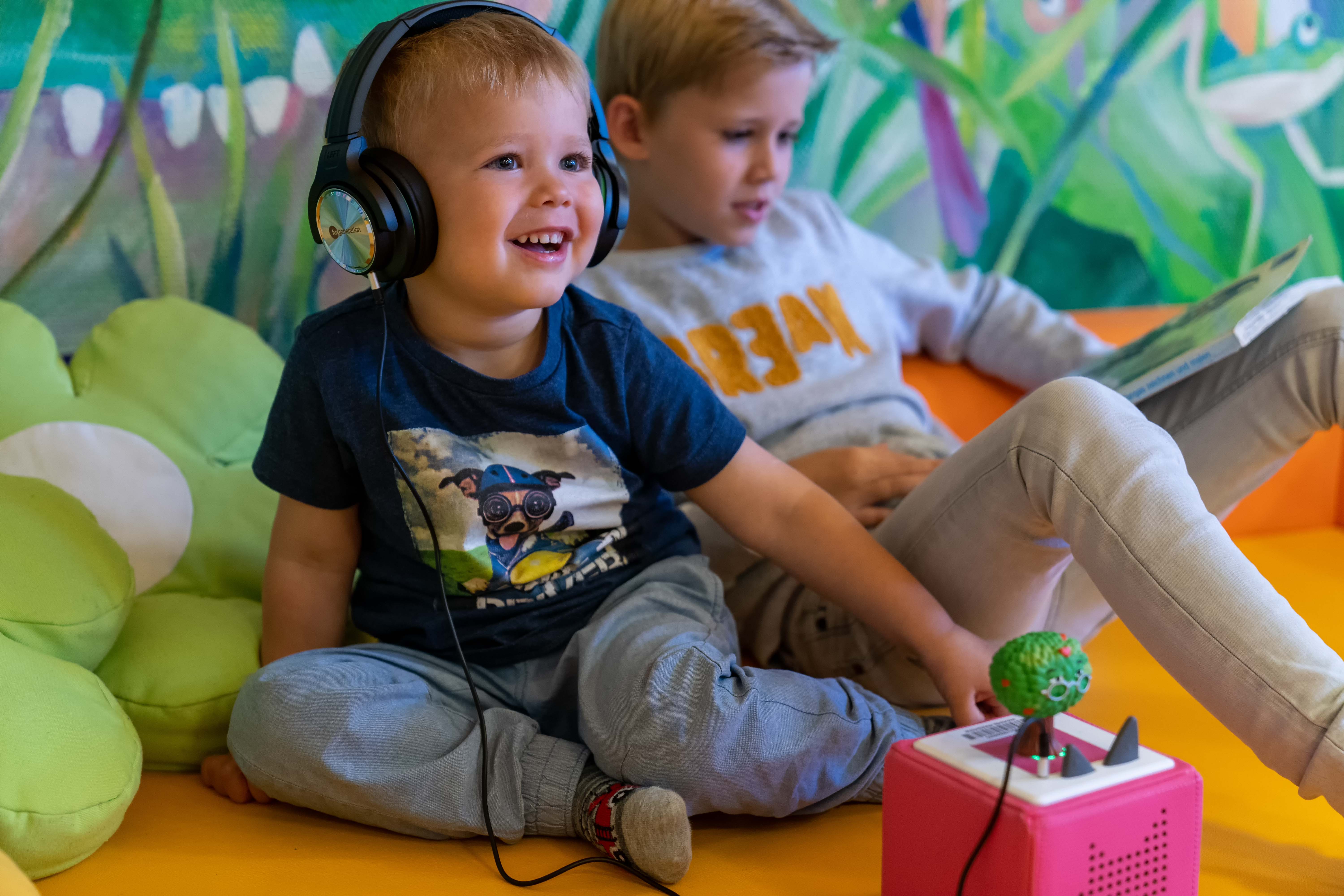 Ein Junge mit Kopfhörern sitzt vor einer Toniebox und lächelt
